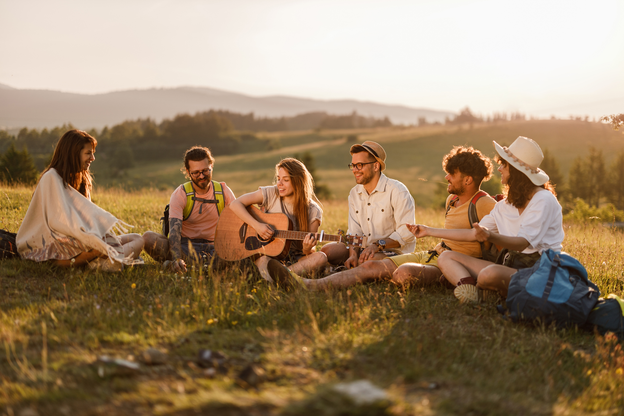 Group of happy hikers enjoying in guitar music while resting on a hill.